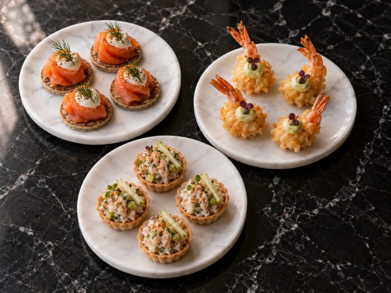 Smoked salmon blinis, tempura prawns and crab tartlets on three white plates