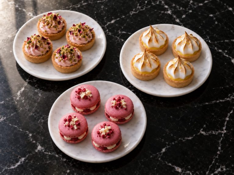 Pistachio rose tartlets, lemon meringue tartlets and raspberry macarons on three white plates