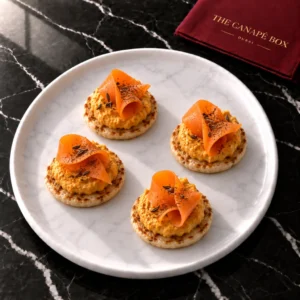 Four portions of Carrot & Orange Hummus on Caraway Crisp on a white marble plate