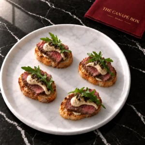 Four portions of Beef Tenderloin & Truffle Crostini on a white marble plate