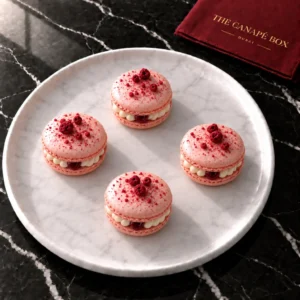 Four raspberry and white chocolate macarons resting flat on a white marble plate