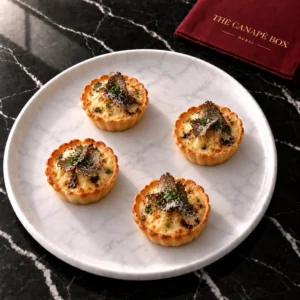 Four portions of Truffle & Parmesan Custard Tartlet on a white marble plate