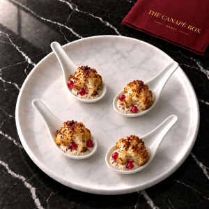 Four portions of Cauliflower & Tahini Bite with Pomegranate on a white marble plate